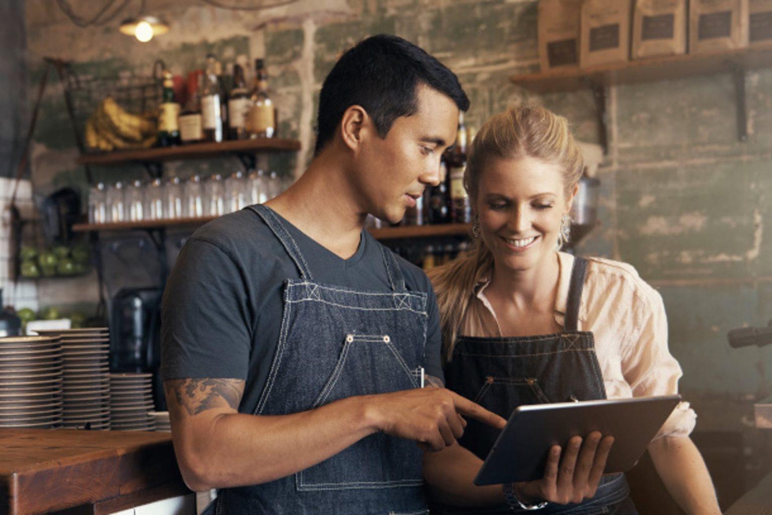 Resengo - Een horecamedewerker toont zijn collega het reserveringssysteem op een iPad, terwijl ze samen werken aan een efficiënte bediening van gasten.