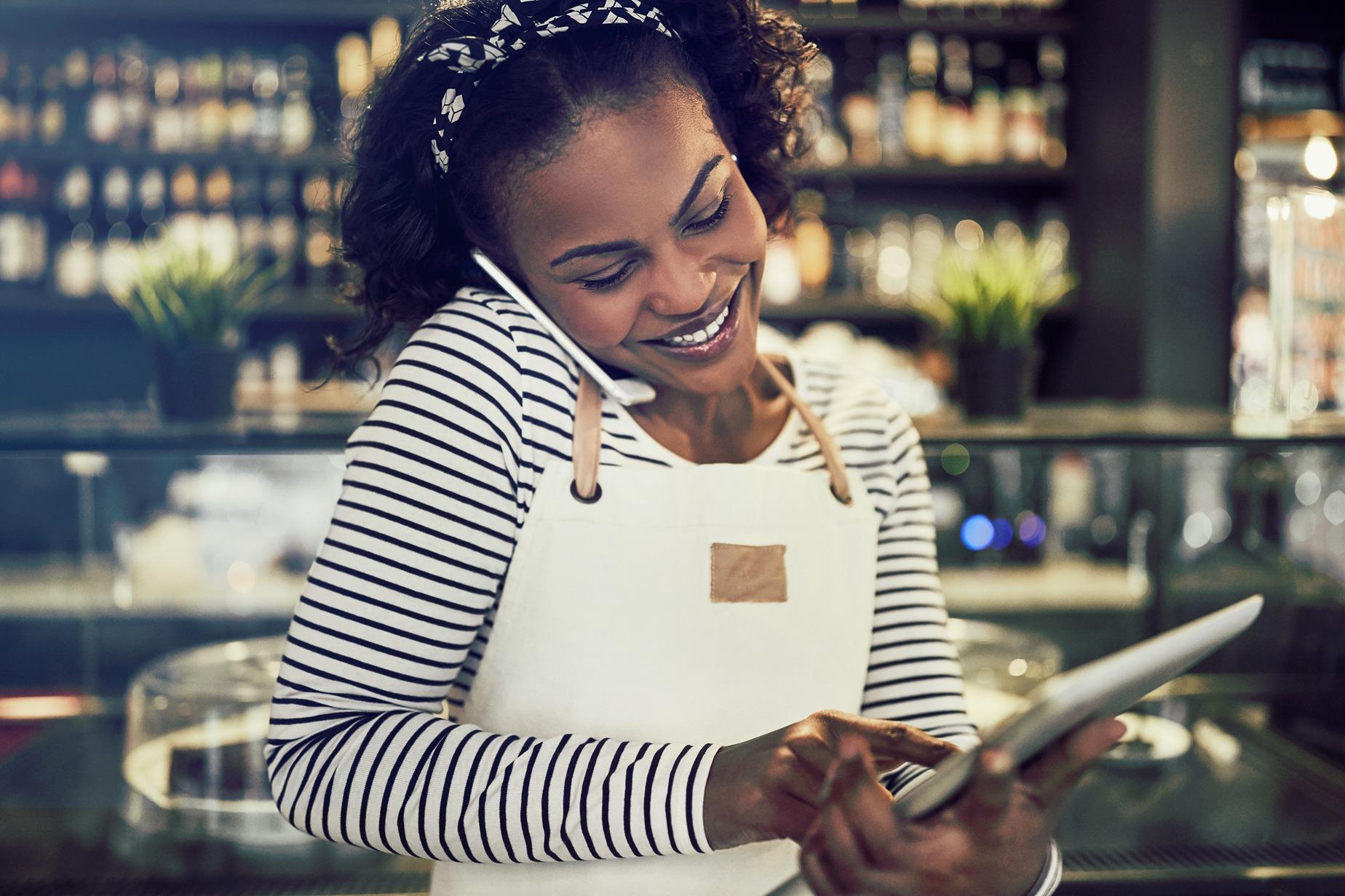 Resengo - Smiling woman hangs on the phone while entering an order on her tablet.